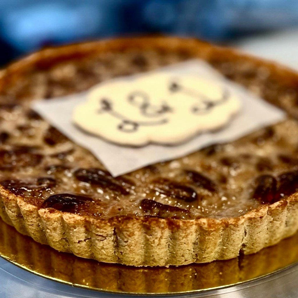 A close-up of a pecan pie featuring a decorative topping with a white cloud-shaped label.